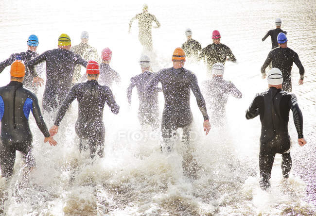 Triatletas seguros y fuertes en trajes de neopreno corriendo hacia el océano - foto de stock