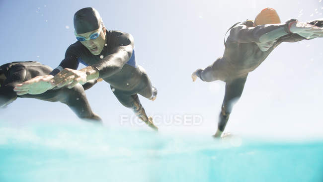 Confident and strong triathletes in wetsuits running into ocean — Stock Photo