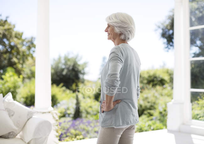 Счастливая пожилая женщина, стоящая на патио, вид сбоку — стоковое фото