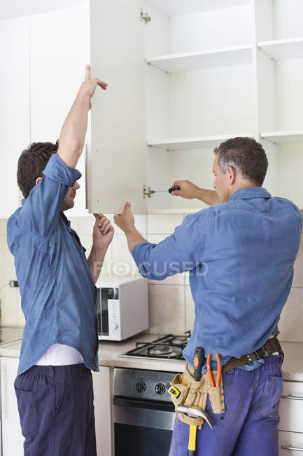 Skillful caucasian workers installing cabinets in kitchen — Stock Photo