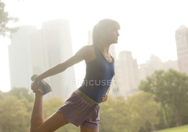 Вид збоку жіночого бігуна, що тягнеться в міському парку — стокове фото