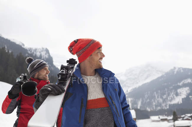 Улыбающиеся мужчины, несущие лыжи у подножия горы — стоковое фото