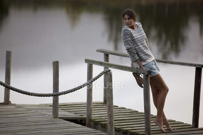 Donna appoggiata su ringhiera sul molo sul lago — Foto stock