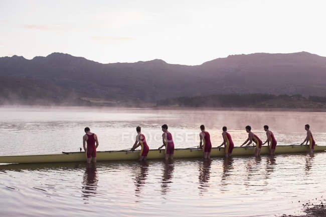 Rowing crew placing scull in lake at dawn — Stock Photo