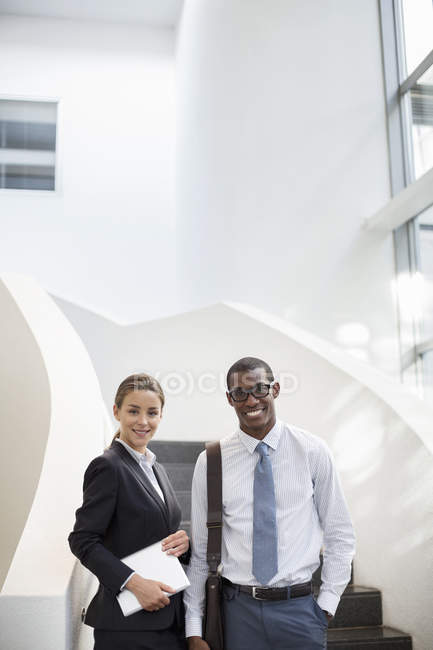 Portrait of smiling businessman and businesswoman at stairs at modern office — Stock Photo