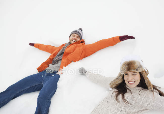 Portrait of happy couple making snow angels — Stock Photo