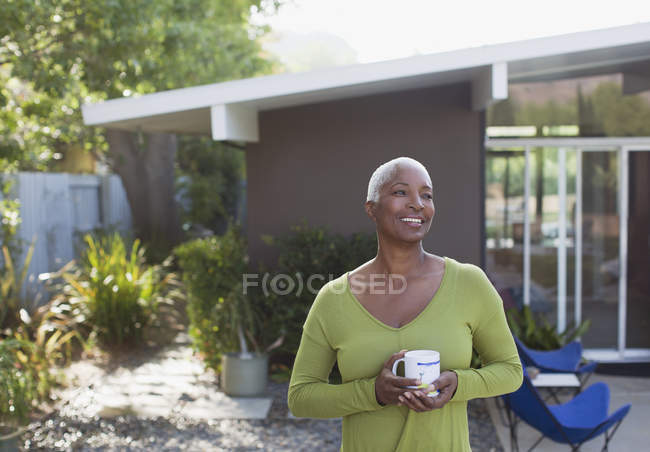 Пожилая женщина пьет кофе на заднем дворе — стоковое фото
