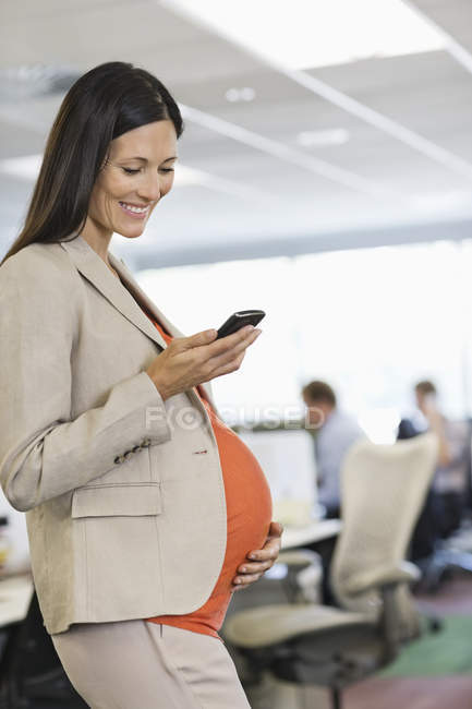 Беременная деловая женщина, использующая мобильный телефон — стоковое фото