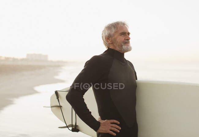 Surfista più anziano che trasporta bordo sulla spiaggia — Foto stock