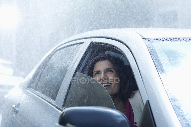 Улыбающаяся деловая женщина в машине смотрит вверх на дождь — стоковое фото