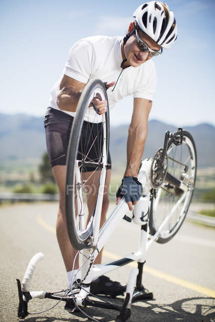 Hombre ajustando bicicleta en carretera rural - foto de stock