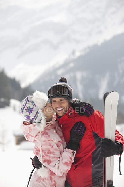 Glückliches Paar mit Skiern küsst sich im verschneiten Feld — Stockfoto