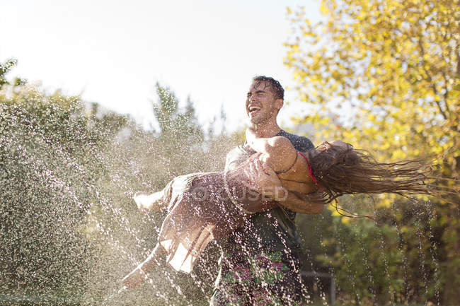 Junges Paar spielt in Sprinkleranlage im Hinterhof — Stockfoto