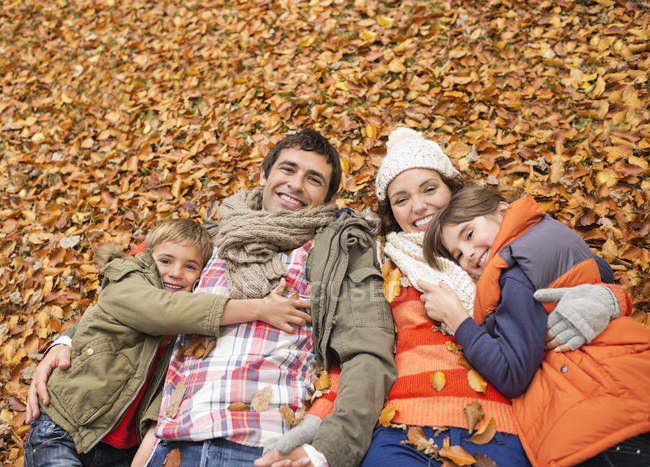 Smiling family laying in autumn leaves — Stock Photo