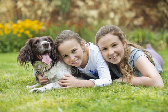 Усміхнені дівчата розслабляються з собакою на газоні — стокове фото