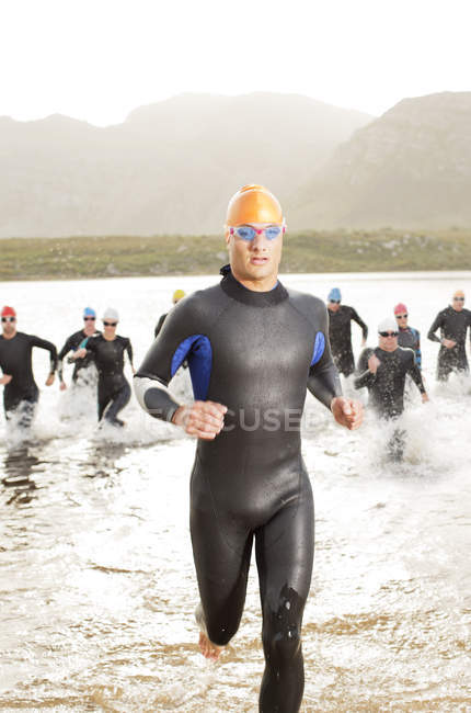 Triatletas confiantes e fortes em roupa de mergulho correndo em ondas — Fotografia de Stock