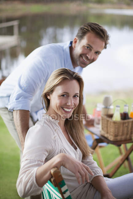 Портрет улыбающейся пары, наслаждающейся пикником на берегу озера — стоковое фото