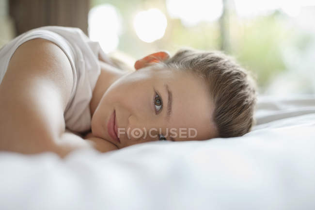 Улыбающаяся девушка лежит на кровати дома и смотрит в камеру — стоковое фото