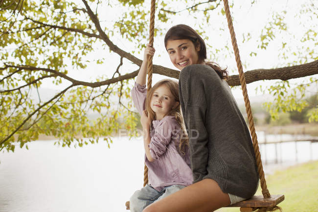 Портрет матери и дочери на качелях у озера — стоковое фото