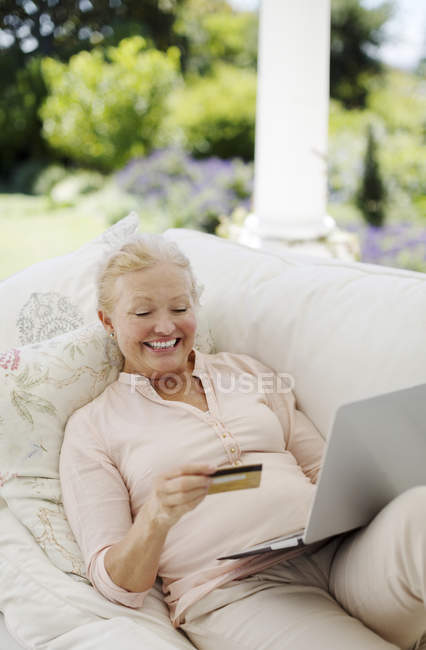 Seniorin kauft online auf Terrassensofa ein — Stockfoto