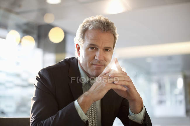 Retrato de empresario confiado con las manos cerradas en la oficina moderna - foto de stock