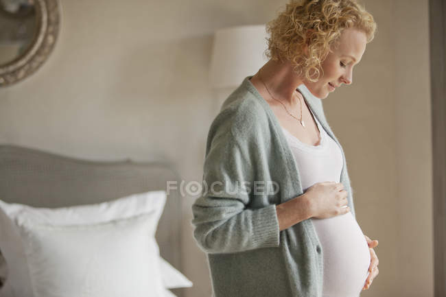 Lächelnde Schwangere berührt Bauch im Schlafzimmer — Stockfoto