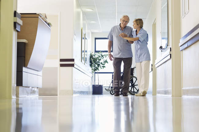 Медсестра помогает пациенту ходить по коридору больницы — стоковое фото