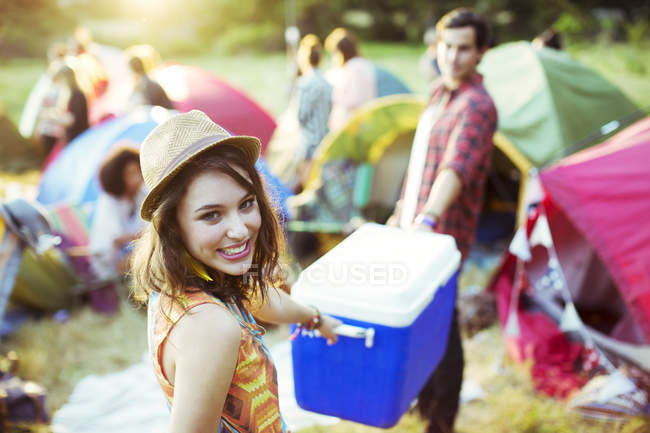 Portrait of woman helping man carry cooler outside tents at music festival — Stock Photo