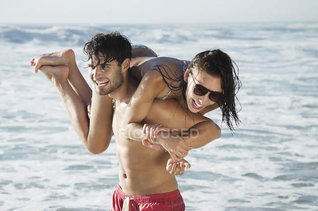 Hombre feliz llevando a la mujer en la playa - foto de stock