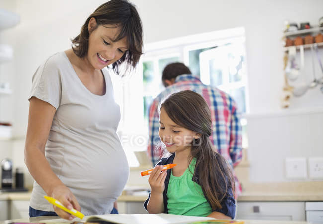 Madre embarazada ayudando a su hija con la tarea - foto de stock