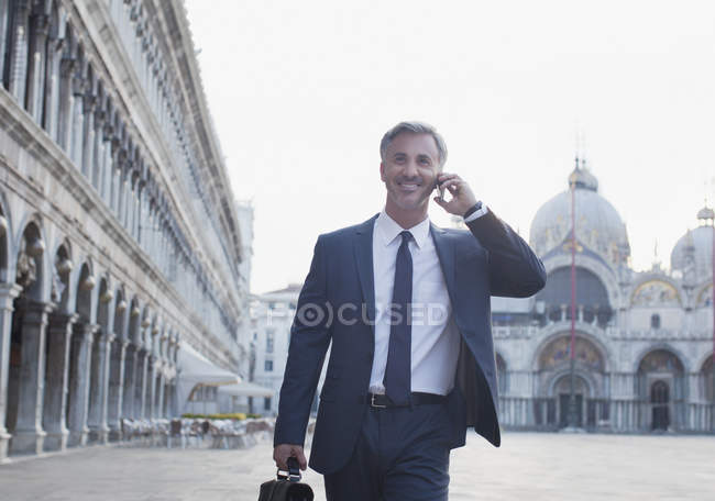 Улыбающийся бизнесмен разговаривает по мобильному телефону и ходит по площади Святого Марка в Венеции — стоковое фото
