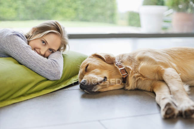Mujer sonriente que se relaja con el perro en el suelo en casa moderna - foto de stock