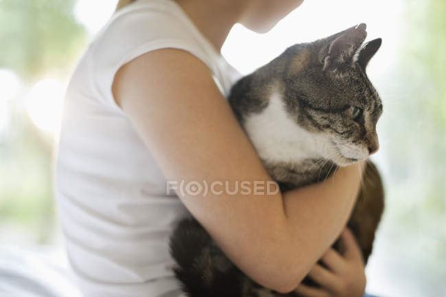 Girl holding cat indoors, cropped image — Stock Photo