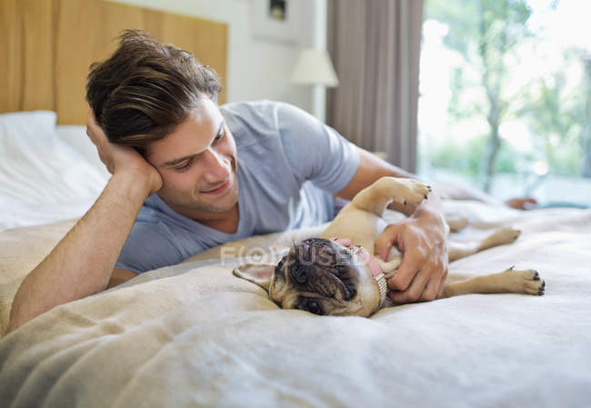 Чоловік кидає собаку на ліжко в сучасному будинку — стокове фото