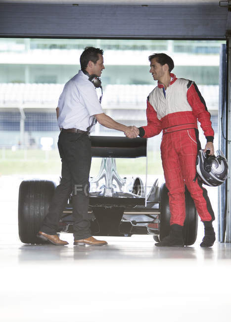 Racer and manager shaking hands in garage — Stock Photo