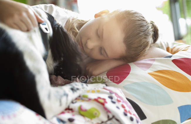 Усміхнена дівчина пестить собаку в ліжку в сучасному будинку — стокове фото