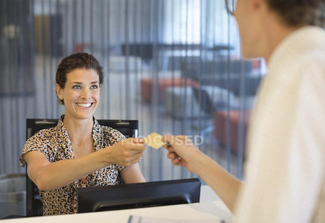 Imprenditrice che consegna carta di credito a un collega in un ufficio moderno — Foto stock