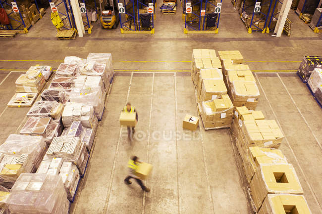 Vista borrosa de los trabajadores que transportan cajas en el almacén - foto de stock
