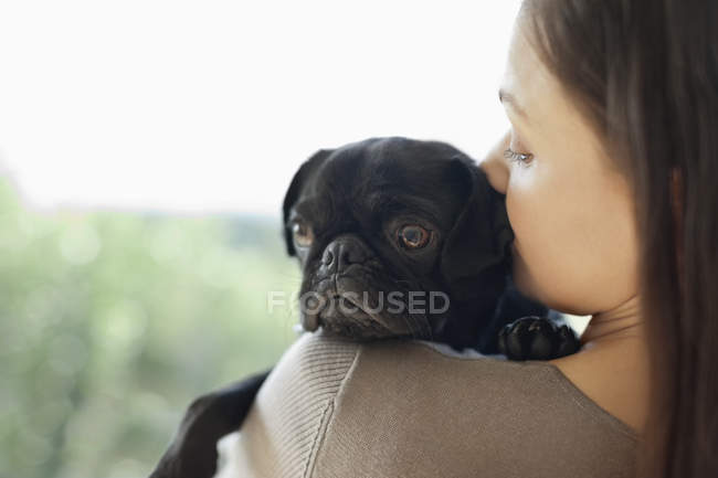 Девушка целует собаку на плече в современном доме — стоковое фото