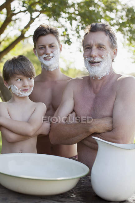 Retrato de hombres de varias generaciones con los brazos cruzados y crema de afeitar en las caras - foto de stock