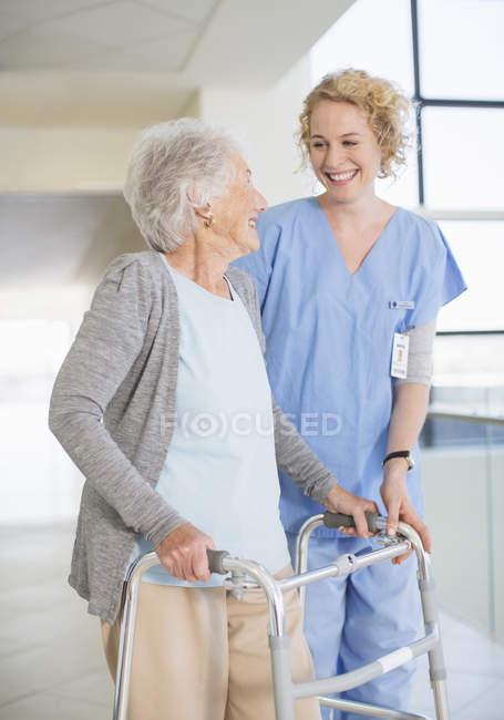 Senior patient with walker smiling at nurse in hospital corridor — Stock Photo