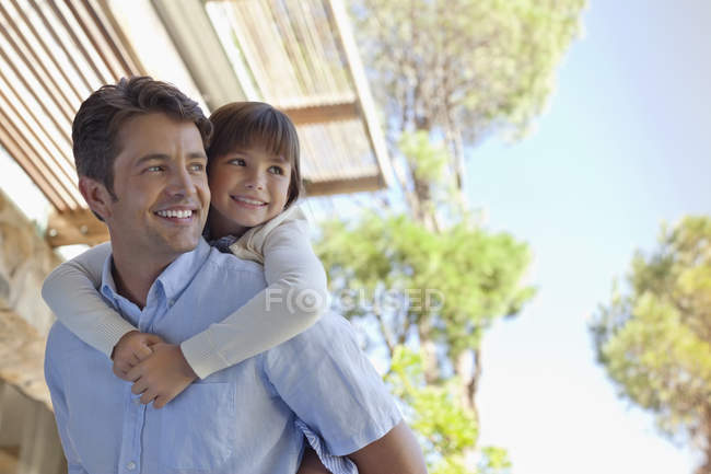 Father carrying daughter piggy back outdoors — Stock Photo