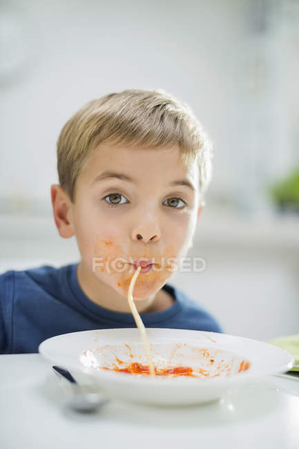 Chico sorbiendo espaguetis en la mesa - foto de stock