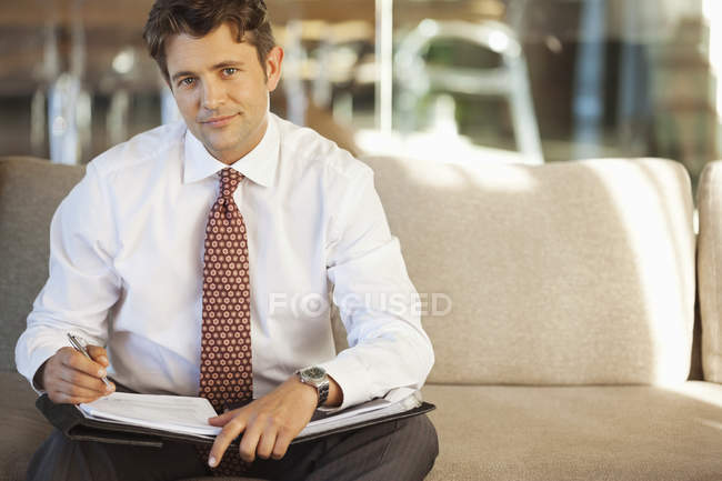Businessman making notes on sofa — Stock Photo