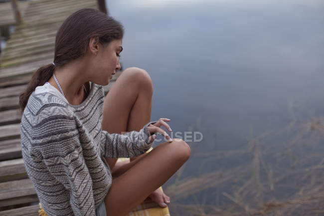 Femme pensive assise sur le quai au-dessus du lac — Photo de stock