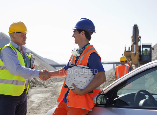 Worker and businessman shaking hands in quarry — Stock Photo