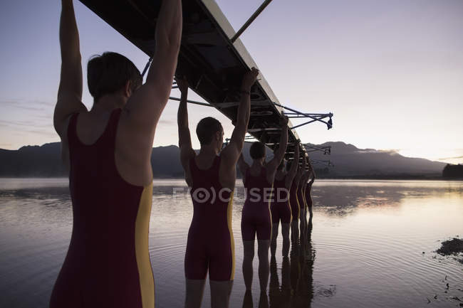 Rowing team carrying boat overhead into lake — Stock Photo