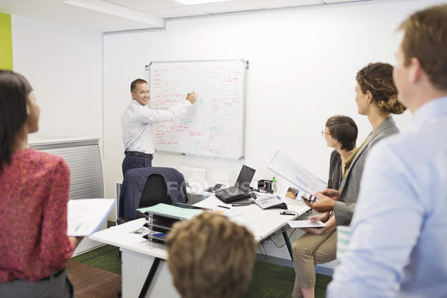 Businessman drawing on whiteboard in meeting at modern office — Stock Photo