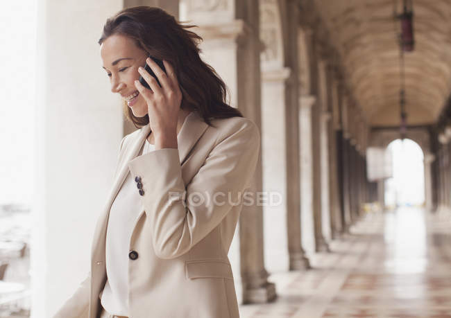 Усміхнена бізнес-леді розмовляє по мобільному телефону в коридорі — стокове фото