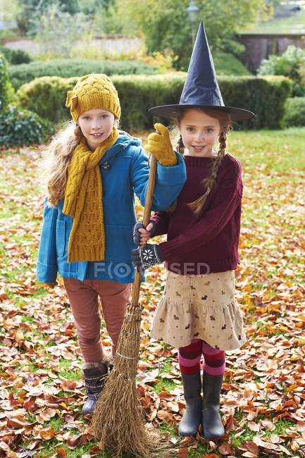 Girls playing with witch hat and broom outdoors — Stock Photo
